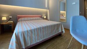 A hotel room with a bed, bedside tables, a chair, a mirror, and a wall-mounted light fixture. - Delta Park (Porto Viro)