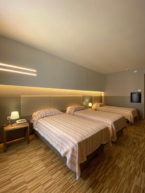 Habitación de hotel con dos camas, una mesita de noche con lámpara, televisor de pantalla plana montado en la pared y suelo de madera.
