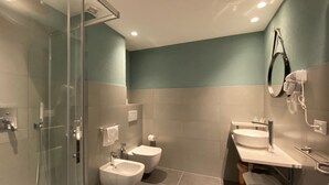 A modern bathroom with a glass shower enclosure, a bidet, a toilet, and a vanity with a mirror and hairdryer. - Delta Park (Porto Viro)