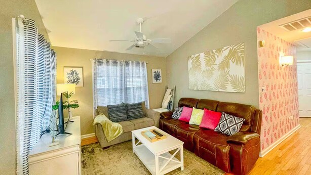 A living room with a sofa, a coffee table, a ceiling fan, and a patterned wall. - Emmas Beach Hut 2 KING BEDS 3 min to beach (Myrtle Beach)