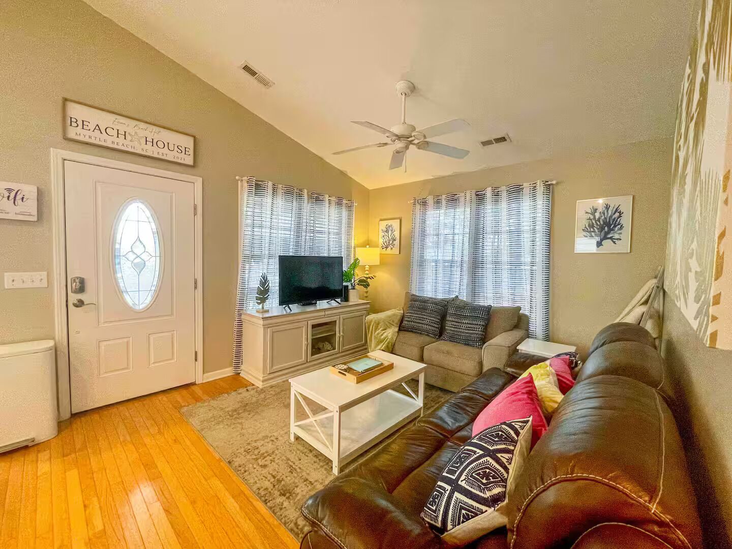 A living room with a television, a white coffee table, a brown leather sofa, and a ceiling fan.