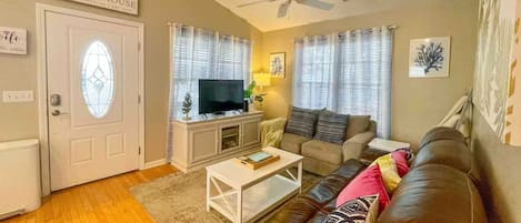 A living room with a television, a white coffee table, a brown leather sofa, and a ceiling fan.