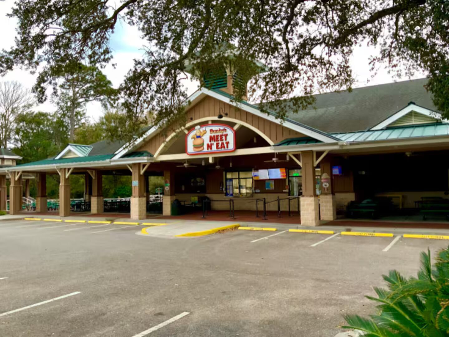 A restaurant with a 'Meet N Eat' sign, outdoor seating, and a parking lot.