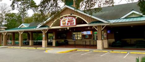 A restaurant with a 'Meet N Eat' sign, outdoor seating, and a parking lot.