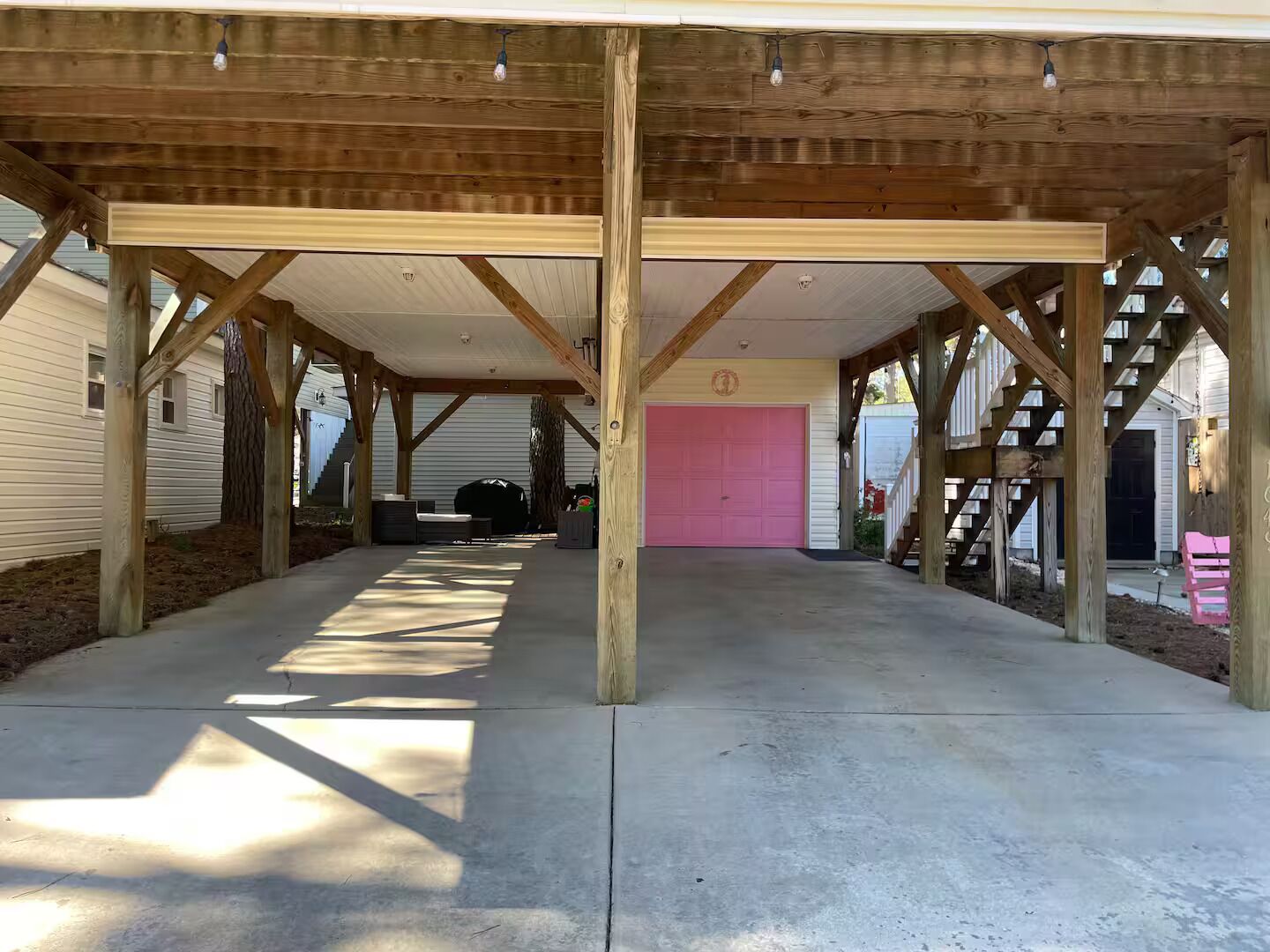 A covered outdoor area with a concrete floor, wooden beams, and a pink garage door.