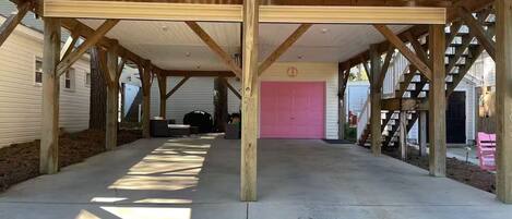 A covered outdoor area with a concrete floor, wooden beams, and a pink garage door.