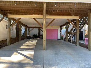 Ett takförsett utomhusområde med ett betonggolv, träbjälkar och en rosa garageport.