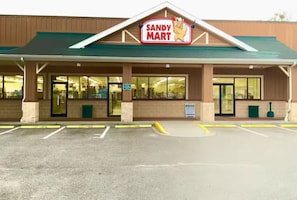 Ein Sandy Mart Geschäft mit einem grünen Dach, großen Fenstern und einem Parkplatz davor.