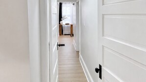 A hallway with white doors and a wooden floor leading to a room with a bed and a window. - Central Moncton 2BR | Walk, Pets & Parking (Moncton)
