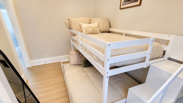 A bunk bed with a mattress and pillows, a wooden floor, and a door. - Central Moncton 2BR | Walk, Pets & Parking (Moncton)