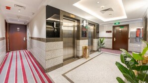 A hotel lobby with a red and white striped carpet, elevators, a reception desk, and a potted plant. - Maysan Rotana El Mysk Fully Renovated (Madinah)