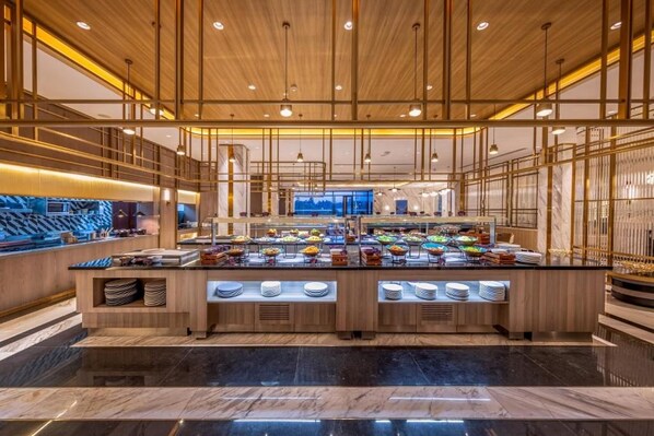 A modern buffet with multiple food stations, a central serving area, and a view of the mountains through the window.