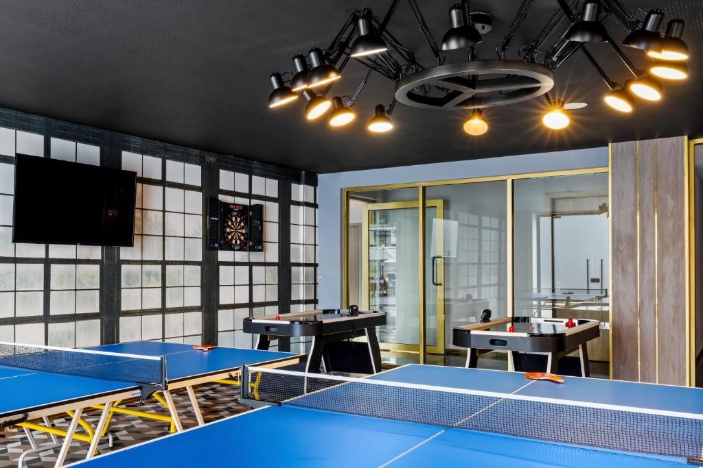 A room with ping pong tables, a dartboard, and a television on the wall.