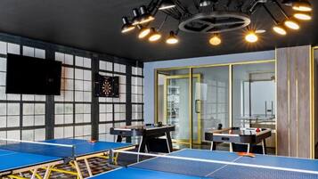 A room with ping pong tables, a dartboard, and a television on the wall.