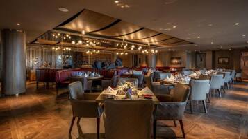 A restaurant with multiple dining tables and chairs, a bar area, and a modern ceiling design.