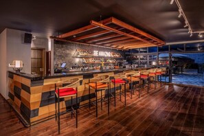 A bar area with a checkered counter, multiple stools with red cushions, and a large window overlooking the outdoor area. - Glee Nairobi Hotel (Nairobi)