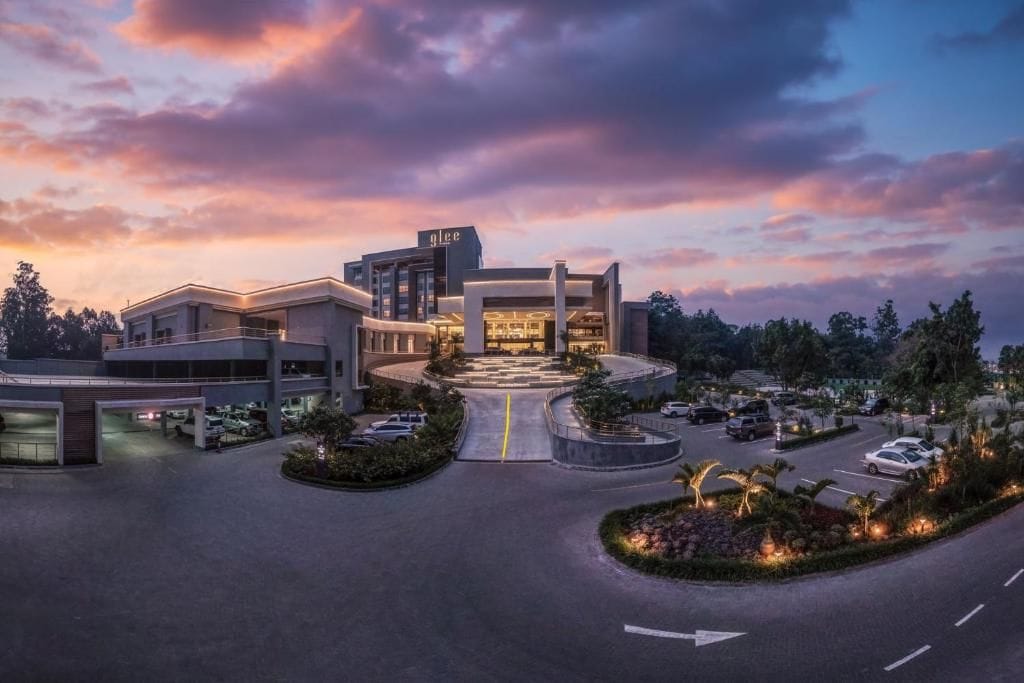 A modern hotel with a central building, multiple parking areas, and landscaped gardens.