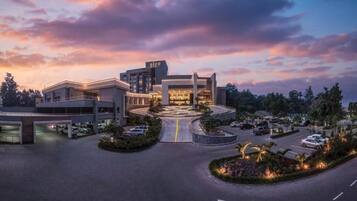 A modern hotel with a central building, multiple parking areas, and landscaped gardens.