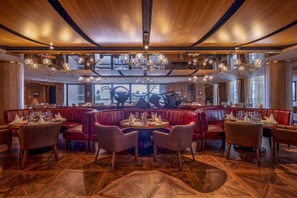 Un restaurante con una mesa redonda central, asientos tapizados en rojo y un techo de madera con candelabros colgantes.