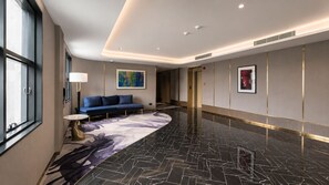 Un hall de hotel con un sofá azul, una mesa redonda y un cuadro abstracto grande en la pared.