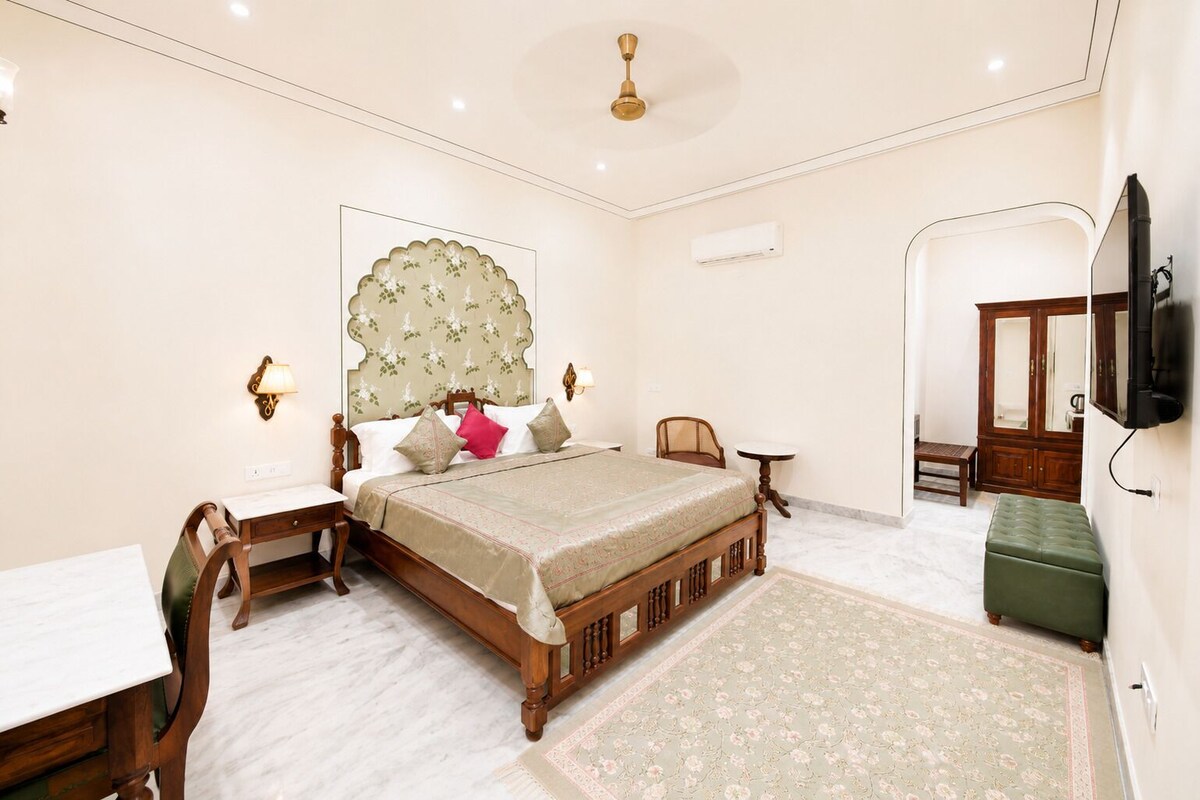 A bedroom with a bed, bedside tables, a desk, a chair, a television, and a wardrobe.