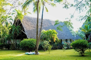A thatched-roof building surrounded by lush greenery and a well-maintained lawn. - Saffron Garden Malindi (Mombasa)