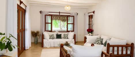 A spacious room with a wooden bed, a sofa, and a window with curtains.