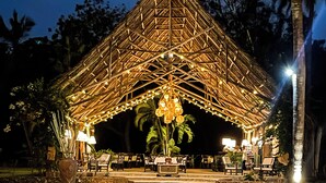 Ein Pavillon mit Strohdach, Lichterketten, ein Pool mit geometrischem Muster und Palmen.