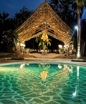 A thatched-roof pavilion with string lights, a pool with a geometric pattern, and palm trees. - Saffron Garden Malindi (Mombasa)