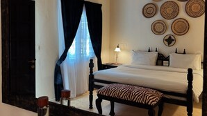 Ein Schlafzimmer mit einem großen Spiegel, einem Bett mit weißer Bettwäsche, einer Bank mit Zeprazebra-Muster und dekorativen Tellern an der Wand.