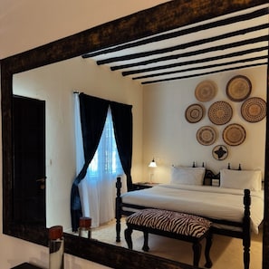 A bedroom with a large mirror, a bed with white bedding, a bench with a zebra pattern, and decorative plates on the wall. - Saffron Garden Malindi (Mombasa)