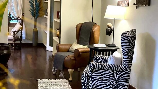 Ein Wohnzimmer mit braunem Ledersofa, einem zebra-gestreiften Sessel, einem kleinen runden Tisch und einer Lampe.
