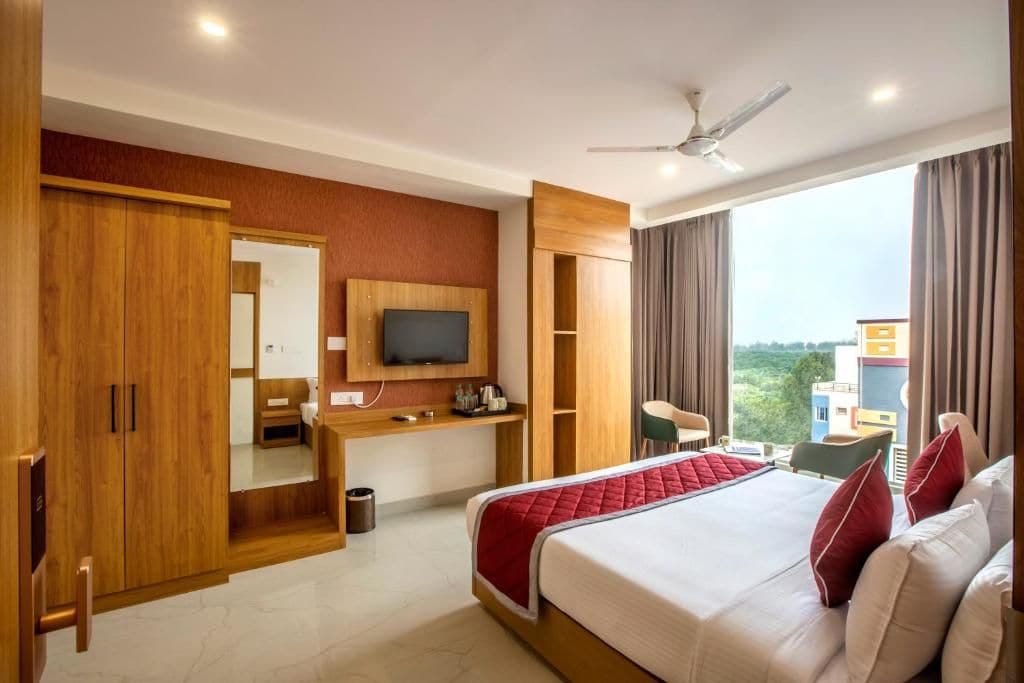 A hotel room with a bed, a desk with a TV, a wardrobe, and a view of the city.