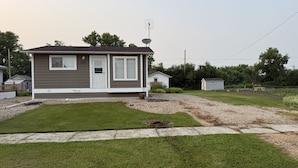 A single-story mobile home with a white door and windows, a satellite dish, and a well-maintained lawn. - Veregin Getaway- Snowmobile trails, Fishing, Hunting, Golf, Lakes, Relaxing (Veregin)