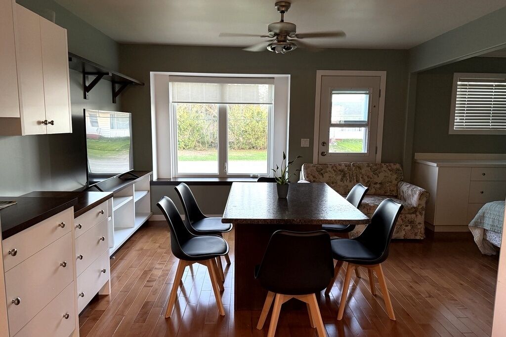 A dining area with a table and chairs, a ceiling fan, and a view of the outdoors through large windows.