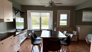A dining area with a table and chairs, a ceiling fan, and a view of the outdoors through large windows. - Veregin Getaway- Snowmobile trails, Fishing, Hunting, Golf, Lakes, Relaxing (Veregin)