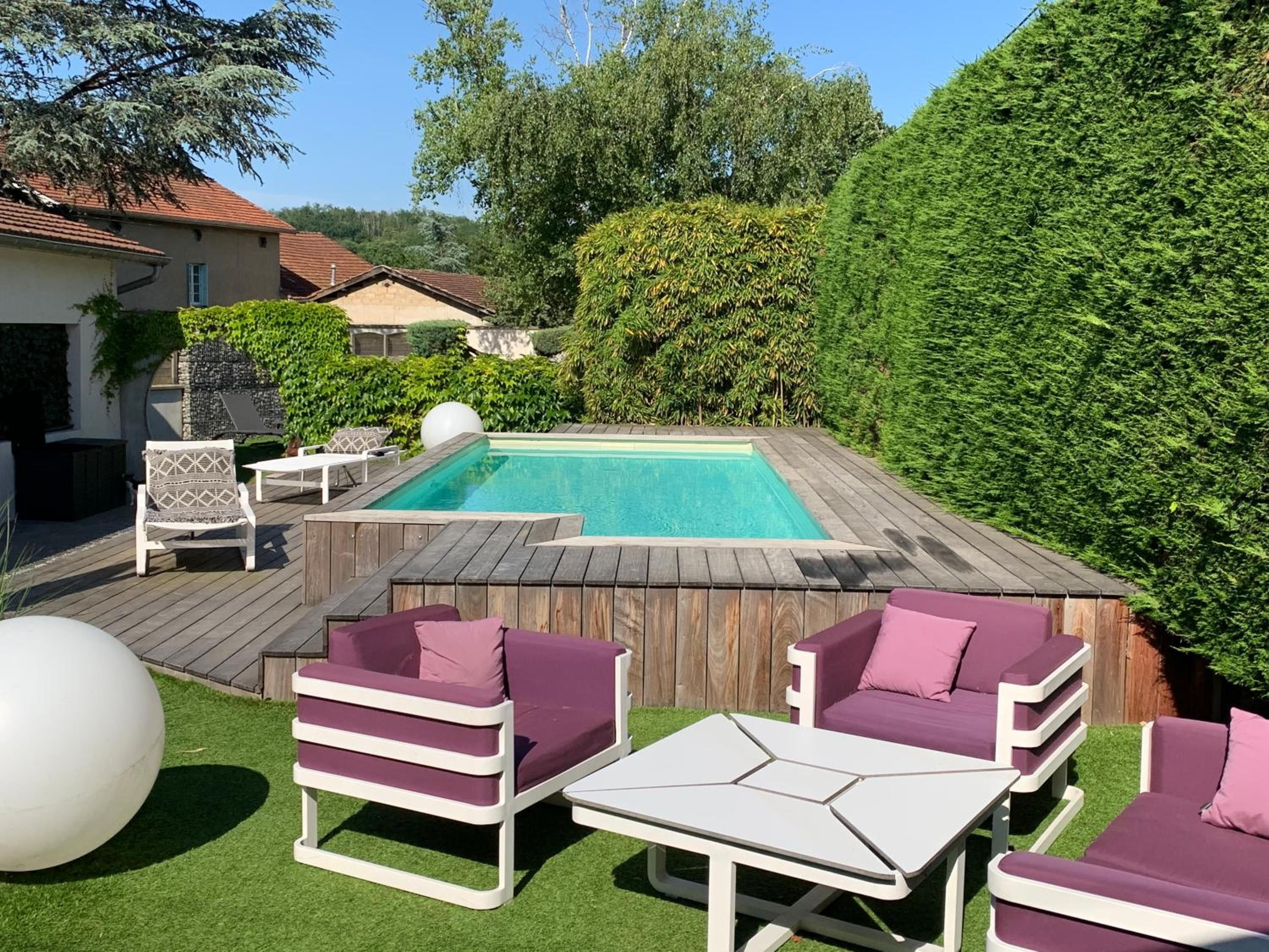 Un patio trasero con piscina, mobiliario exterior y terraza de madera.
