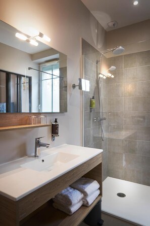Un baño moderno con un espejo grande, un lavabo blanco, una cabina de ducha de vidrio y un perchero para toallas.