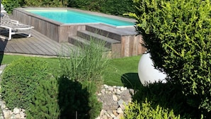 A backyard with a swimming pool, wooden deck, and various plants. - Pont Du Chalon Hôtel And Restaurant (Marges)