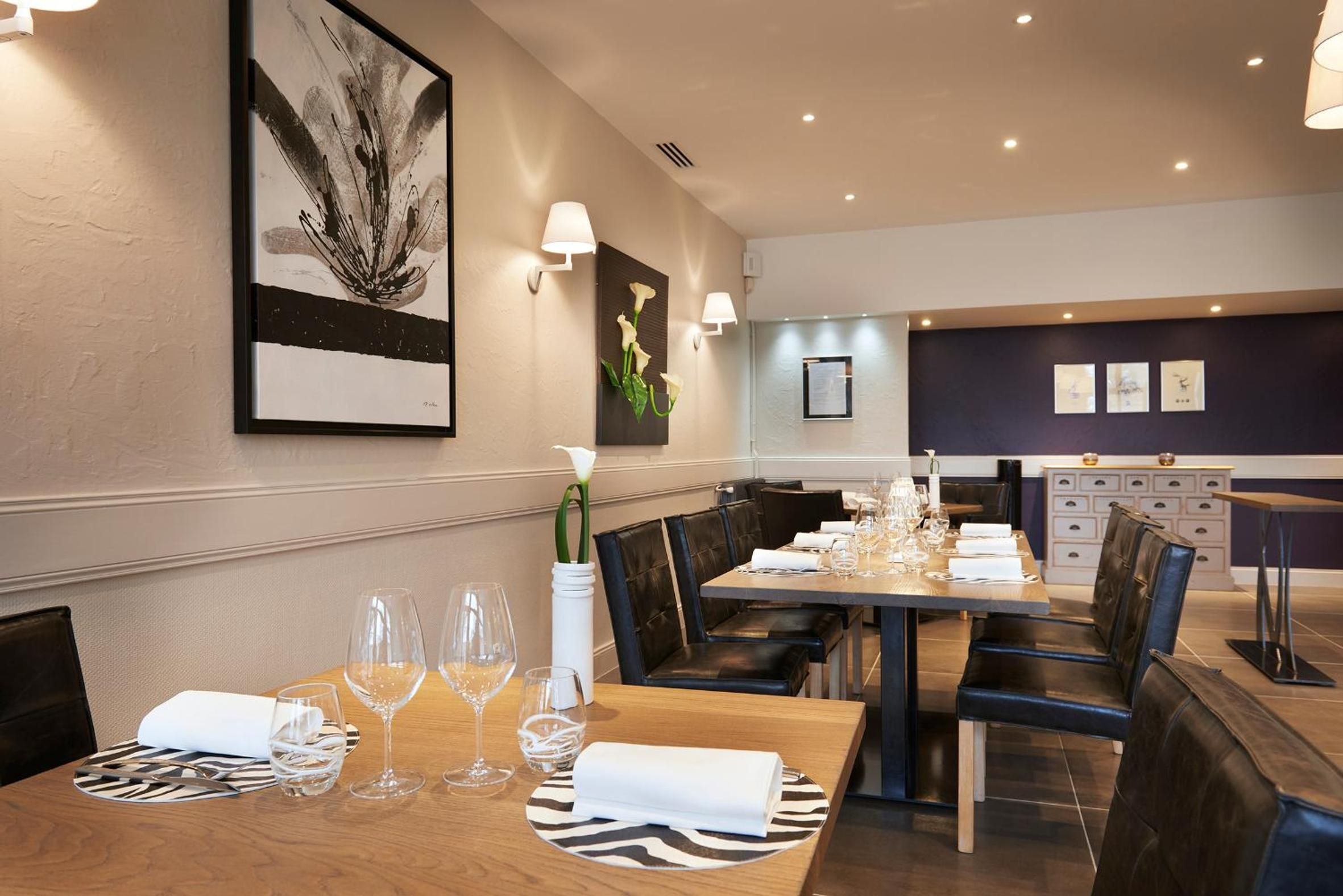 A dining area with a wooden table set for four, surrounded by black leather chairs.