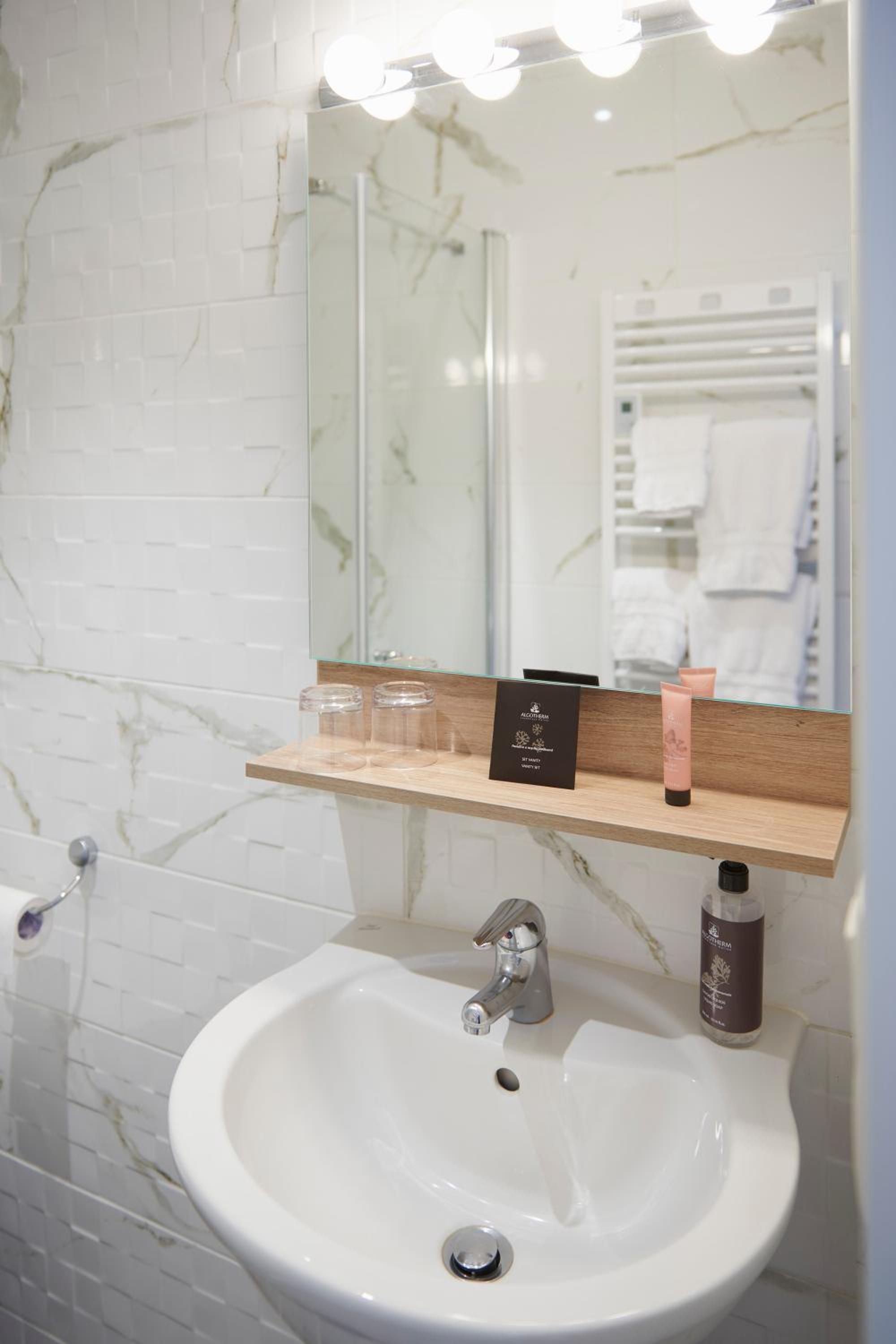 Een badkamer met een witte wastafel, een spiegel met verlichting en een houten plank met toiletartikelen.