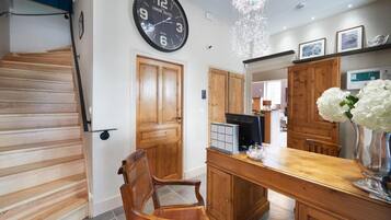 A hotel interior with a wooden staircase, a dining area with a wooden table, chairs, and a clock on the wall.