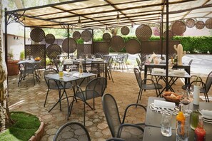 Un café al aire libre con mesas y sillas, una pérgola y paneles decorativos.