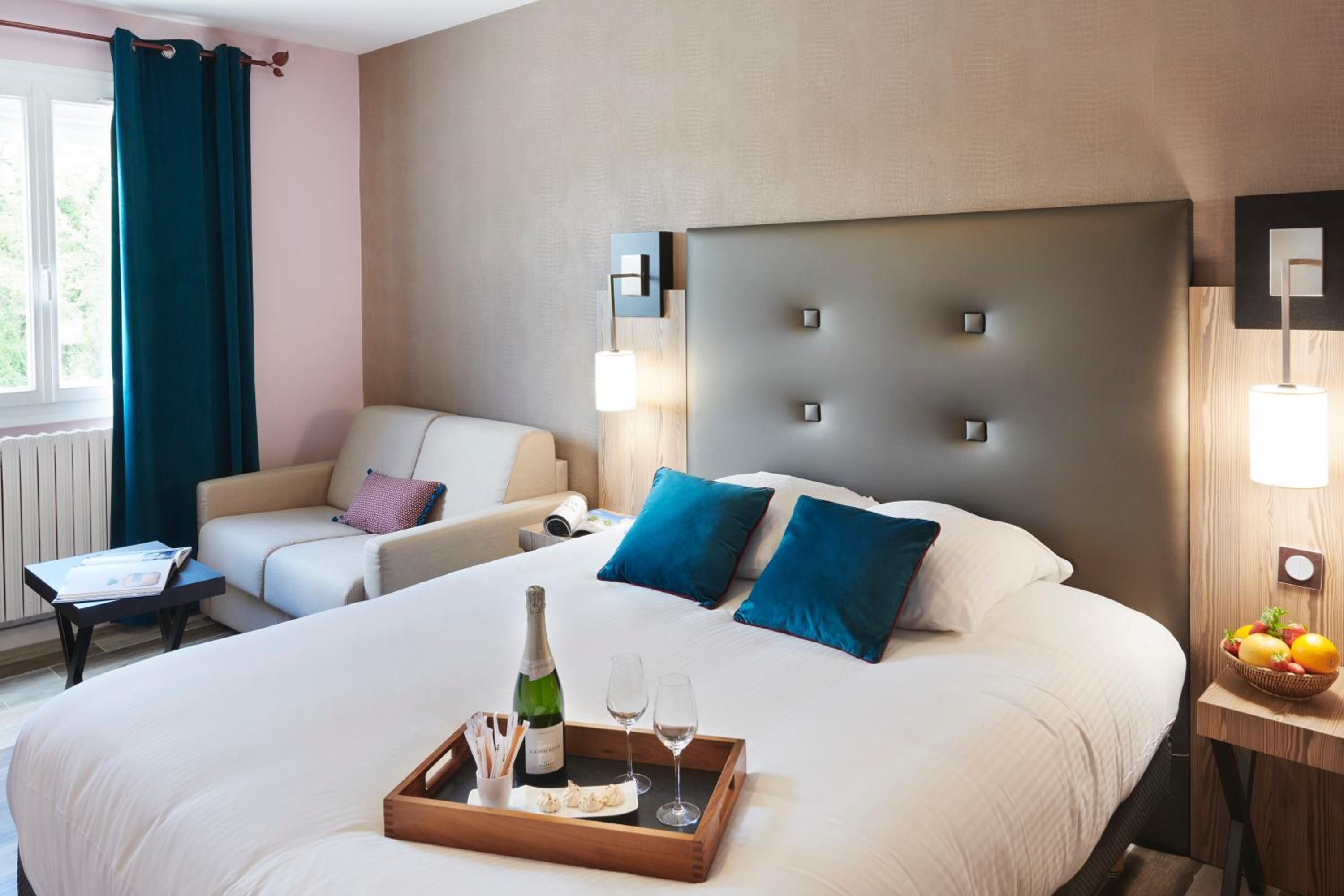 A hotel room with a large bed, two bedside tables, a sofa, and a window with curtains.
