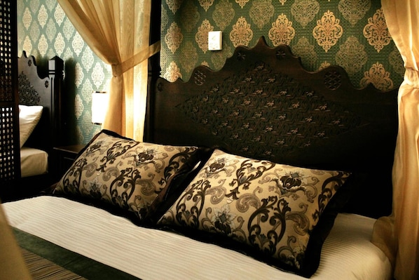 A bed with two patterned pillows, a headboard with a geometric pattern, and a green patterned wall. - Isa Begov Hamam Hotel (Sarajevo)