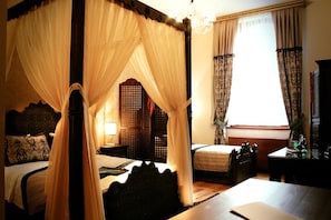 A four-poster canopy bed with a wooden headboard, a bedside table with a lamp, and a window with curtains. - Isa Begov Hamam Hotel (Sarajevo)