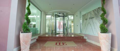 A hotel entrance with a revolving door, a marble floor, and potted plants.
