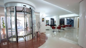 Eine Lobby mit einer Drehtür, einem Empfangsbereich und einer Sitzecke mit roten Stühlen.