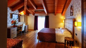 Ein Hotelzimmer mit Holzboden, einem Bett mit gemustertem Überwurf, einem Schreibtisch mit Stuhl, einem Fernseher und einem Fenster mit Vorhängen.