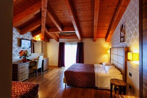 A hotel room with a wooden ceiling, a bed with a patterned bedspread, a desk with a chair, a television, and a window with curtains. - Hotel Eridano (Sannazzaro de Burgondi)